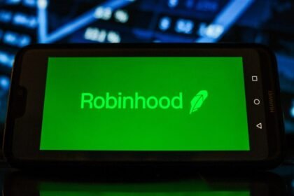 A Robinhood logo seen displayed on a smartphone with the stock market graphic in the background.